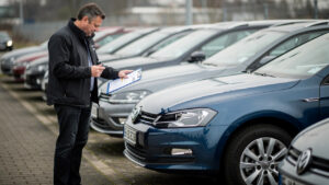 Un homme compare des caractéristiques de voitures sur un parc automobile en Allemagne, avant l’importation vers la France.