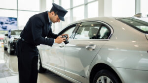 Un chauffeur professionnel examine attentivement la carrosserie d'une berline argentée et la photographie dans une concession automobile.
